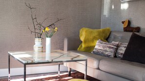 A modern living room with a glass coffee table, a sofa with patterned cushions, and a decorative vase with yellow flowers.