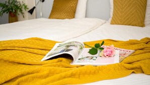 Ein Bett mit gelber Decke, ein Magazin mit einer Rose und Kissen mit Zickzackmuster.