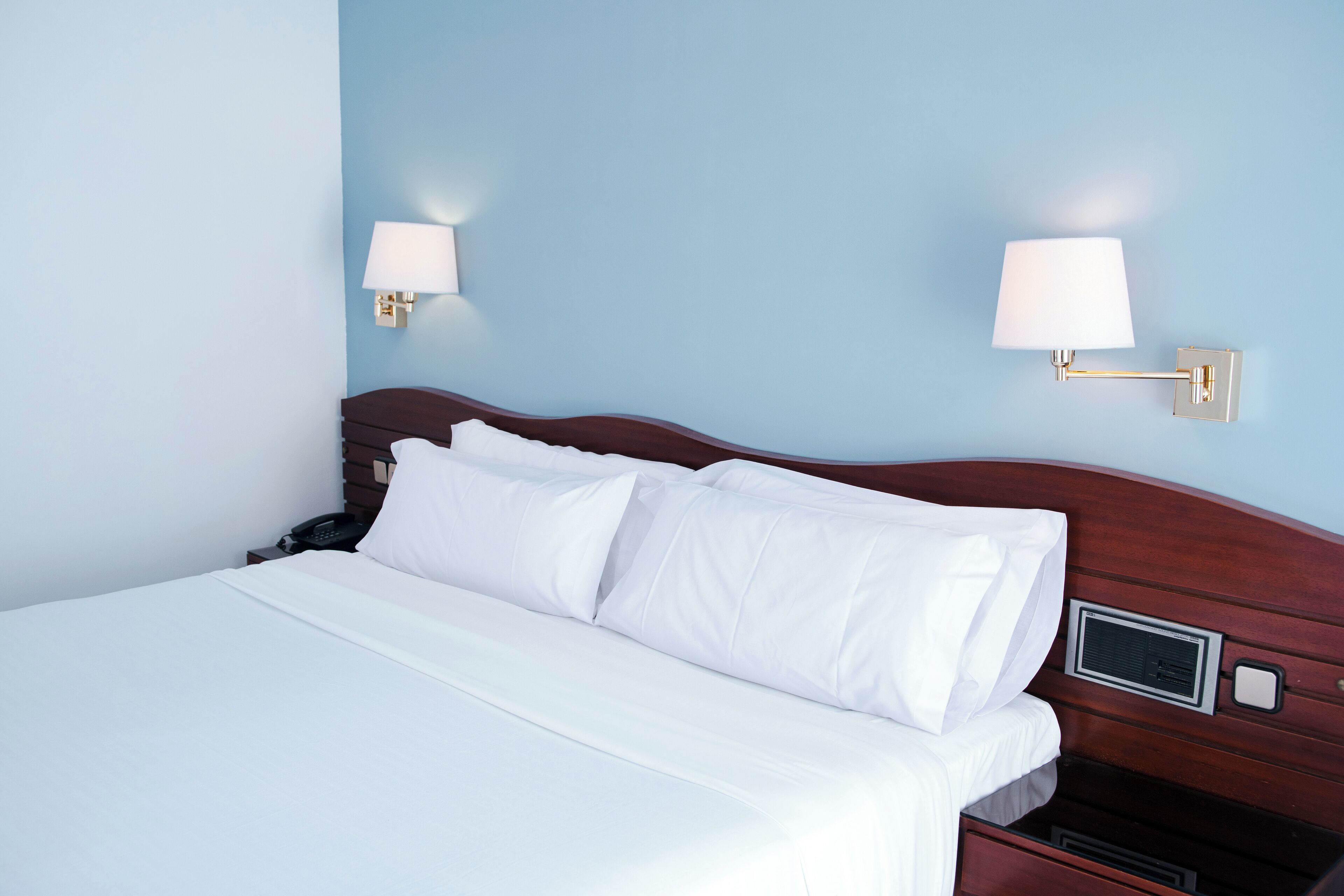 A neatly made bed with white linens in a room with light blue walls.
