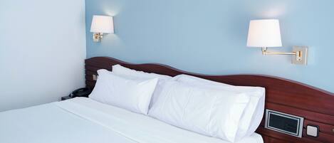 A neatly made bed with white linens in a room with light blue walls.