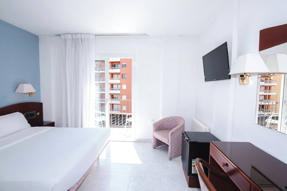 Hotelkamer met een bed, bureau, stoel, televisie en raam met uitzicht op een gebouw.