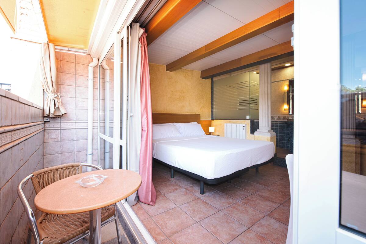 Een kleine hotelkamer met een bed, een tafeltje en een stoel.