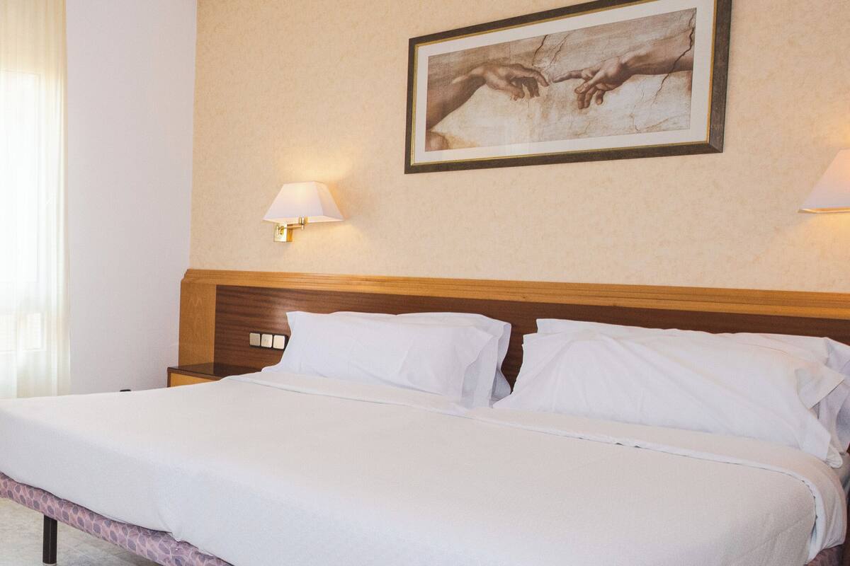 Een groot bed met een houten hoofdbord, twee nachtkastjes met lampen, en een lijstwerk met een kunstwerk aan de muur.