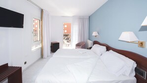 Una habitación de hotel con una cama grande, un televisor montado en la pared, un escritorio y una silla.