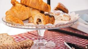 Un soporte de vidrio para pasteles con diversas opciones, incluyendo croissants y un pastel cubierto de chocolate.