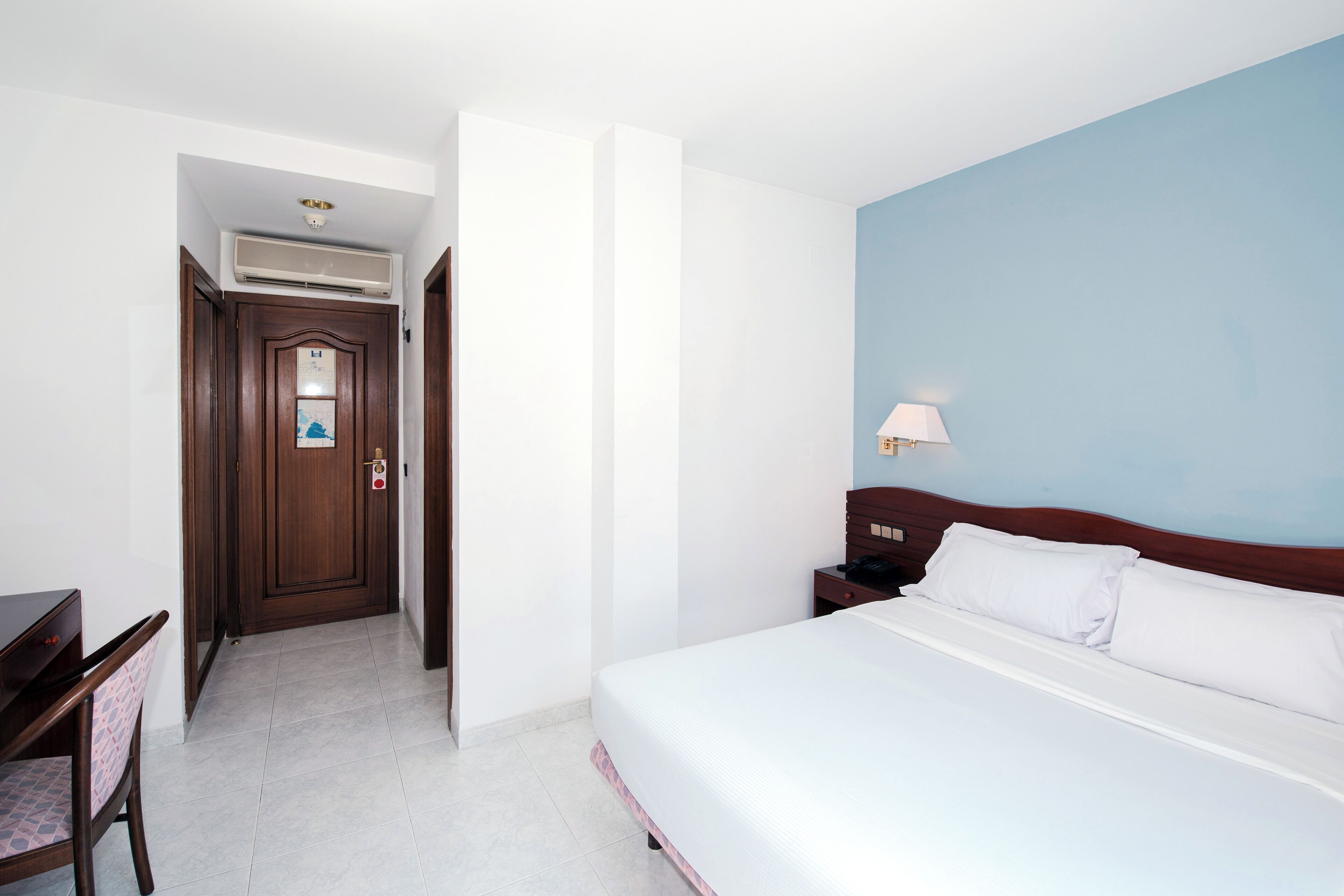 Habitación de hotel con cama, escritorio y silla. Se ve una puerta que da a otra habitación.