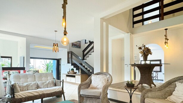 A spacious living area with wicker furniture, a teal coffee table, and a staircase leading to an upper level. - Casa com piscina Praia da Vila Nova (Imbituba)