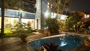 A modern house with a swimming pool, surrounded by tropical plants and a wooden deck. - Casa com piscina Praia da Vila Nova (Imbituba)