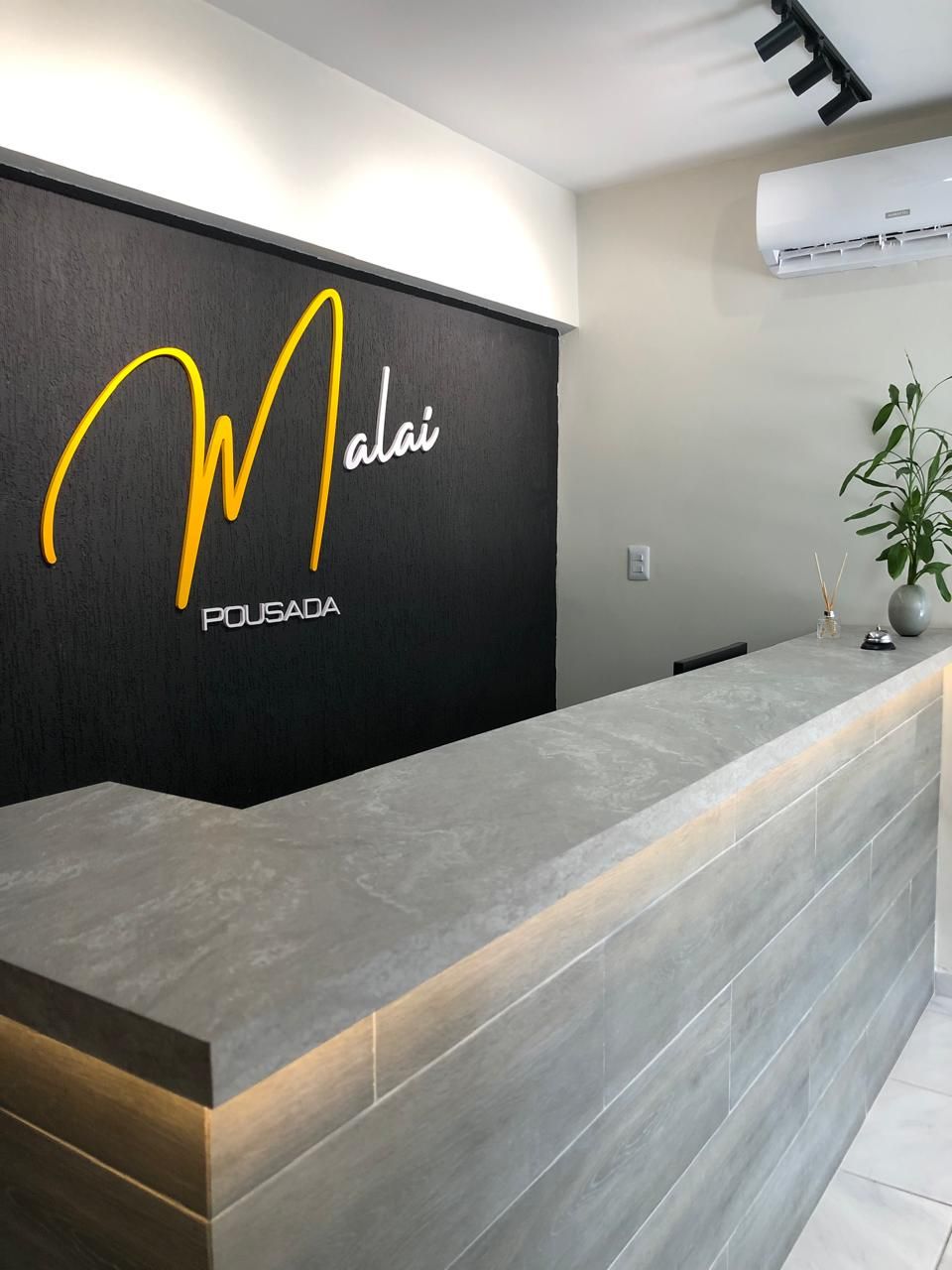 A reception desk with a black wall and a logo that reads "Malai Pousada".