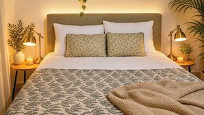 Una cama bien hecha con ropa de cama estampada, dos lámparas de noche y cuadros en la pared.