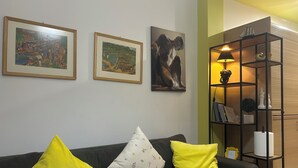 Una sala de estar con un sofá oscuro, cojines amarillos y obras de arte enmarcadas en la pared.