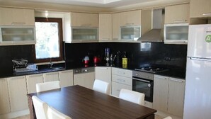 Uma cozinha moderna com armários de madeira clara, bancada escura, fogão de aço inoxidável e geladeira branca.