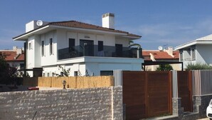Uma casa moderna de dois andares com varanda, antena parabólica e cerca de madeira.