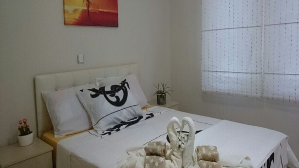 Quarto de hotel com cama, mesa de cabeceira, planta em vaso e pintura na parede.