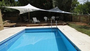 Piscina retangular com deck branco e toldo branco acima.