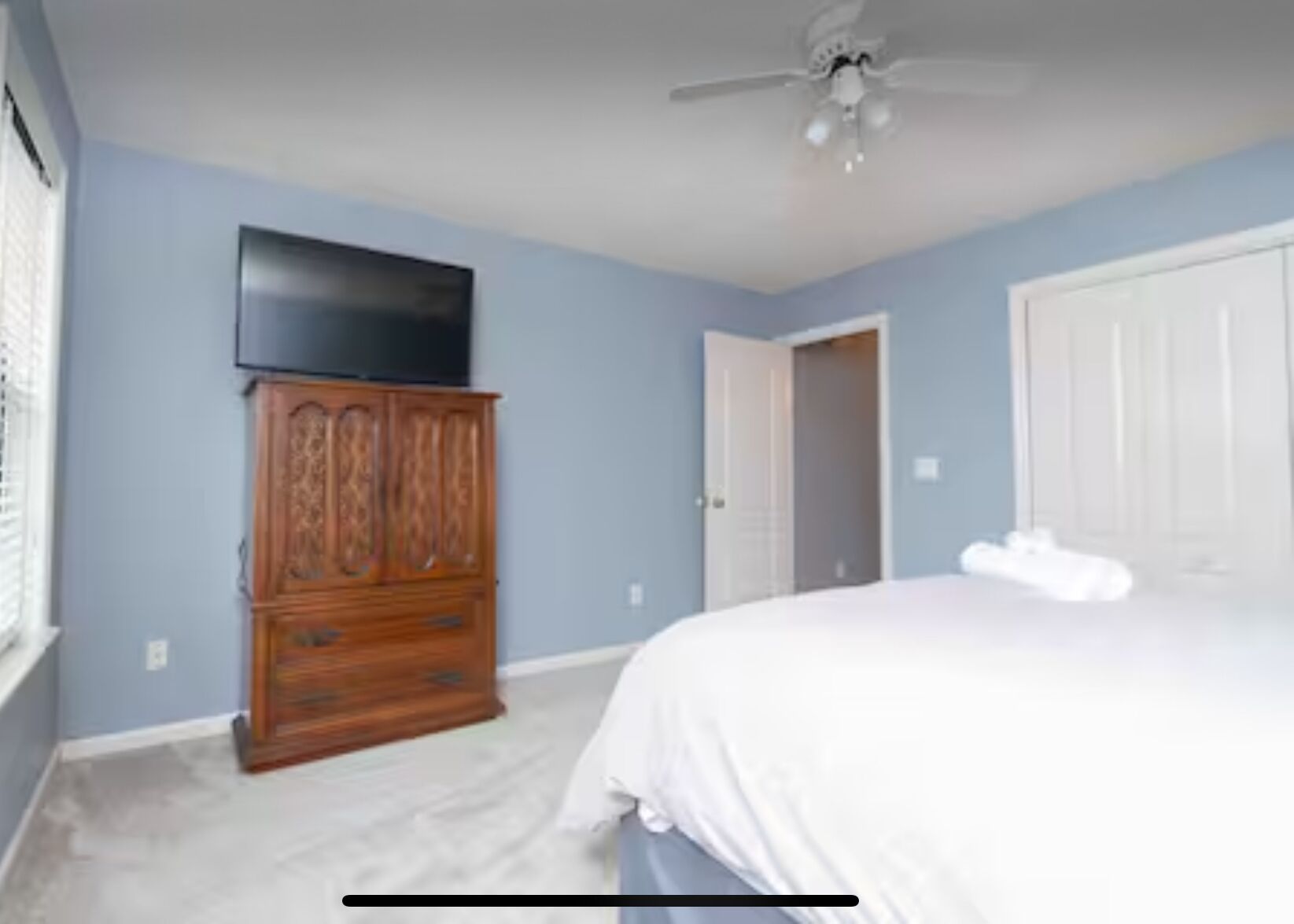 Een slaapkamer met een bed, een houten dressoir, een televisie aan de muur en een plafondventilator.
