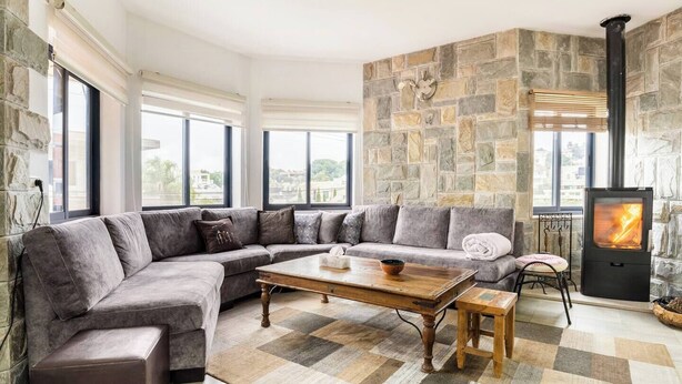 Una sala de estar moderna con una pared de acento de piedra, un sofá seccional, una mesa de centro de madera y un estufa a leña.