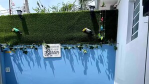 A small outdoor seating area with two chairs and a table, surrounded by artificial grass and a blue wall. - The Retreat - 5 min to Airport (Carolina)