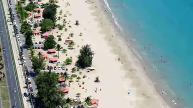 An aerial view of a beach with a road running parallel to it, lined with palm trees and beach umbrellas. - The Retreat - 5 min to Airport (Carolina)