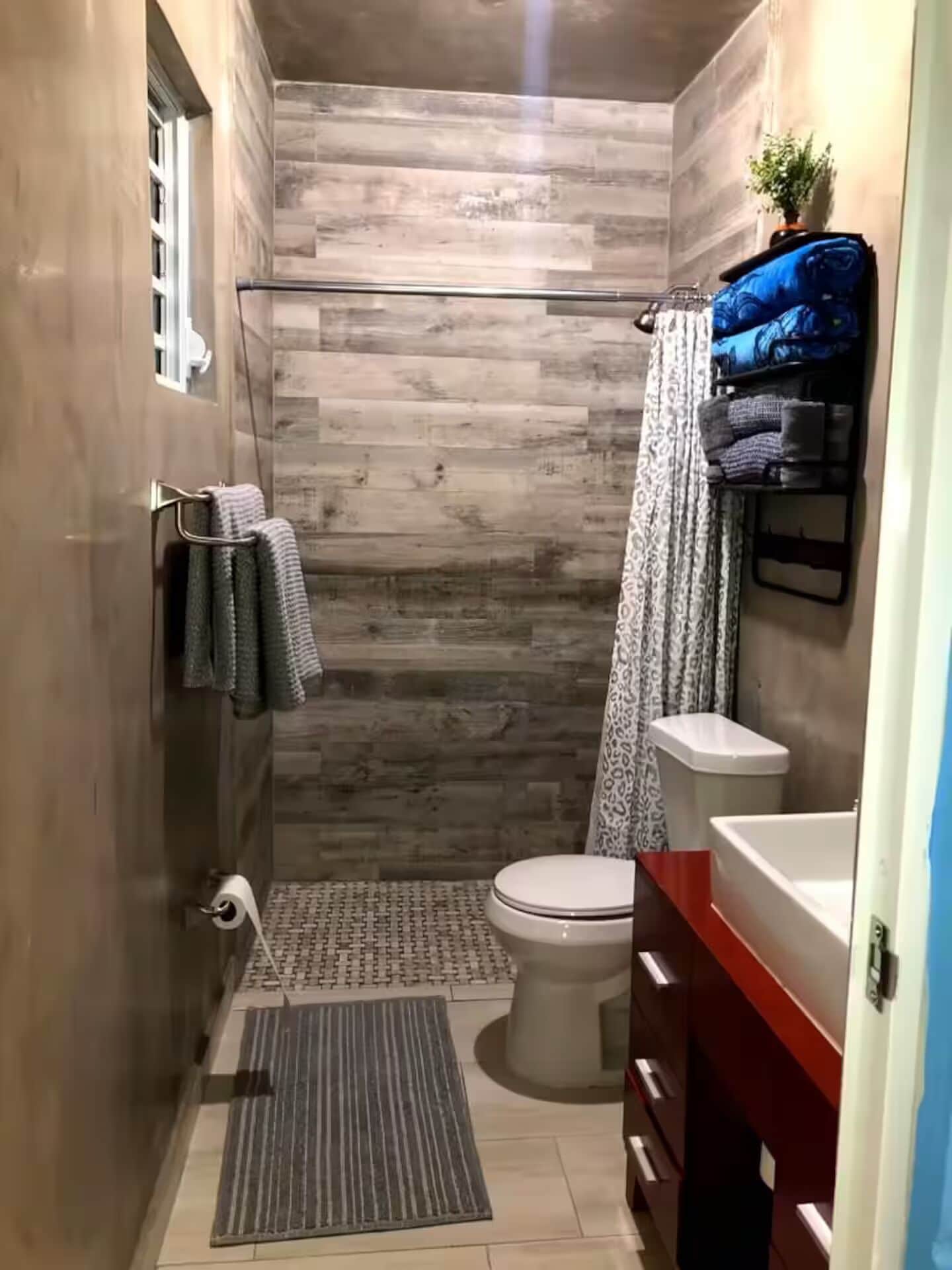 Ein schmales Badezimmer mit Dusche, Toilette und einer kleinen Waschtisch-Ecke.
