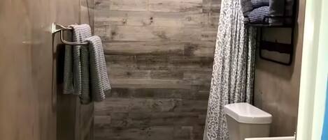 Ein schmales Badezimmer mit Dusche, Toilette und einer kleinen Waschtisch-Ecke.
