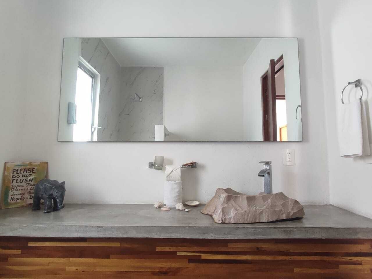 Un bagno con parete in marmo, un ampio specchio, un mobile vanitario in legno, un lavandino e un portasciugamani.