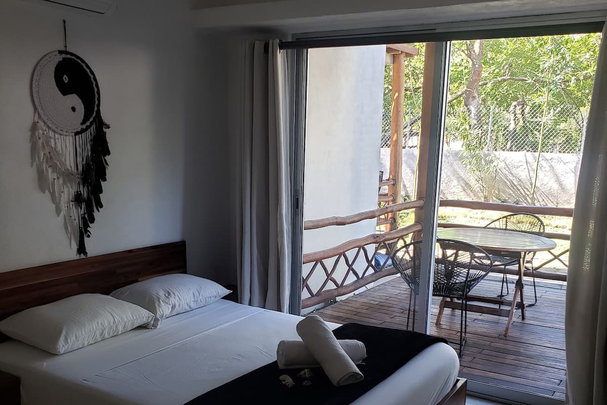 A bedroom with a bed, a ceiling fan, a dreamcatcher, and a view of an outdoor area with a table and chairs.