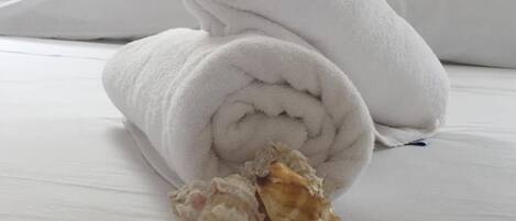 A neatly made bed with white linens and rolled white towels.