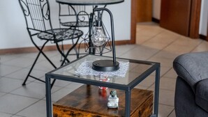 Une table carrée avec un plateau en verre, une base en bois et un cadre en métal, posée sur un sol carrelé.