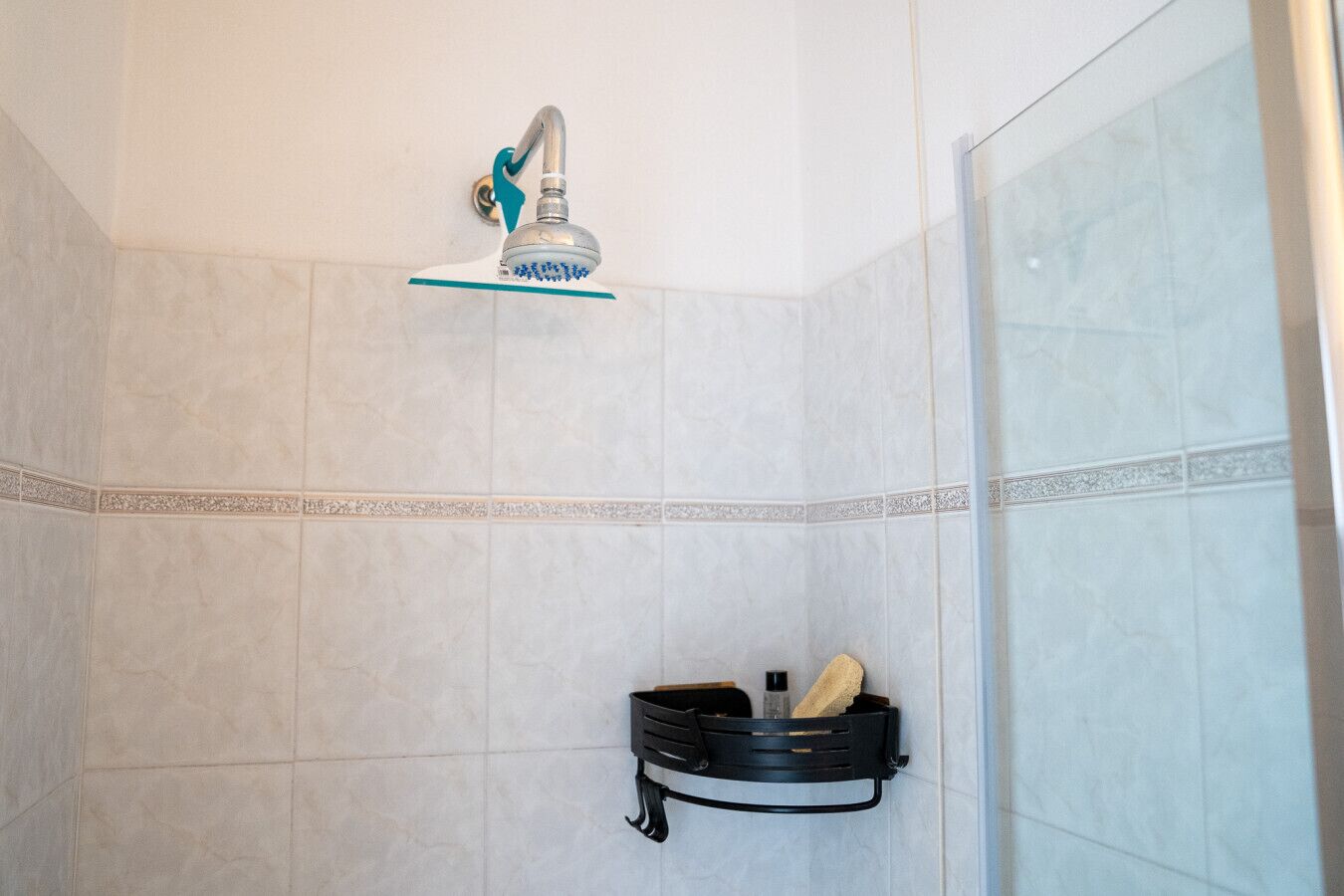 A shower with a handheld showerhead, a glass shower enclosure, and a black towel rack with a towel and a bottle.