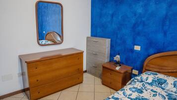 Una camera da letto con una cassettiera in legno, un piccolo mobiletto, un comodino con una lampada e un letto con copriletto floreale.