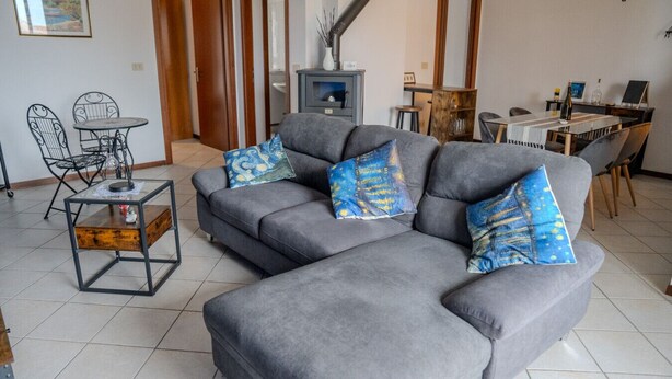 Un salon moderne avec un canapé d’angle gris, une petite table basse en bois et un coin repas comprenant une table et des chaises blanches.
