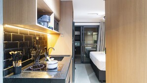 Ein kleines Hotelzimmer mit Küchenzeile, einem Bett und einer Schiebetür zum Badezimmer.