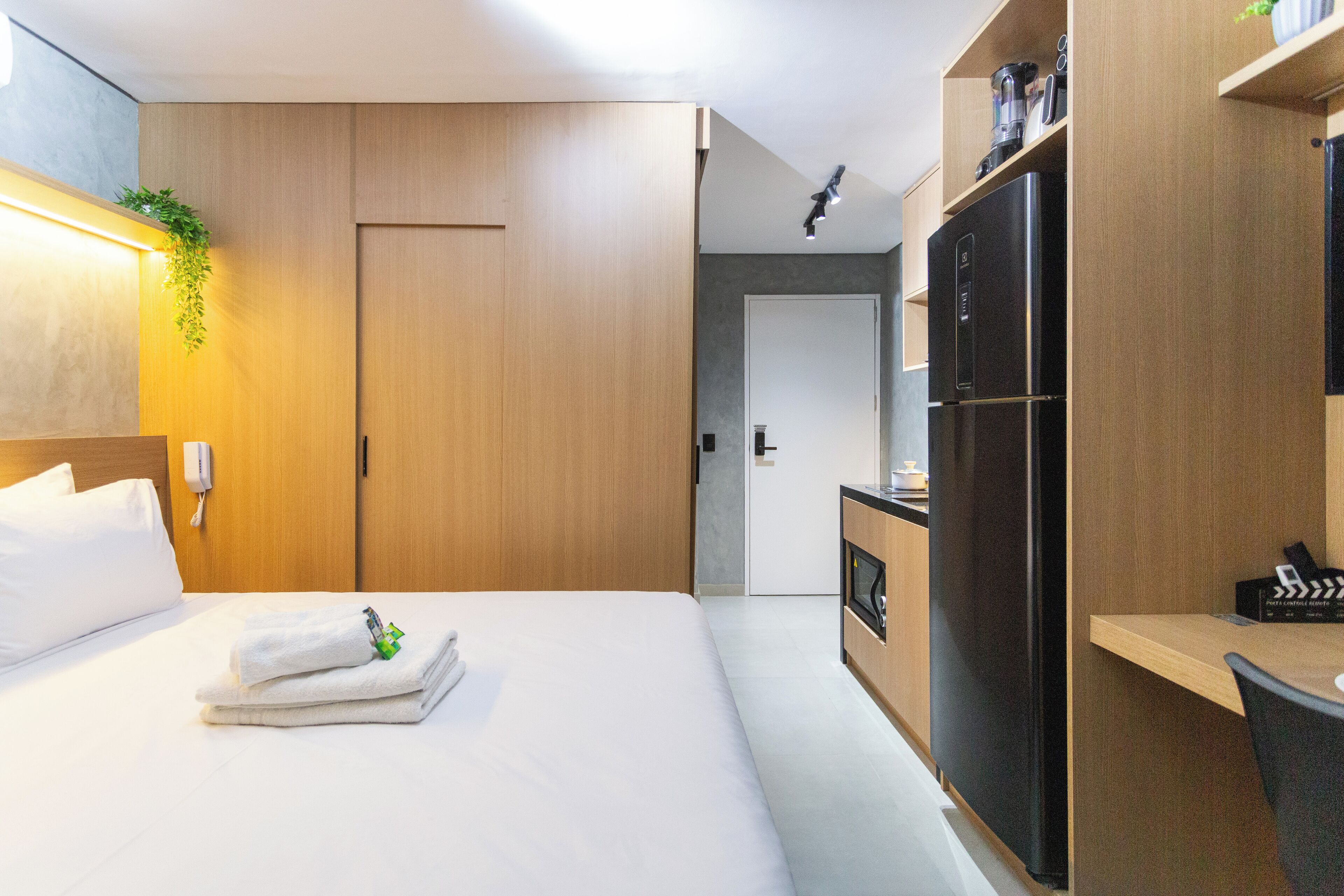A hotel room with a bed, a desk, a refrigerator, and a door leading to a bathroom.