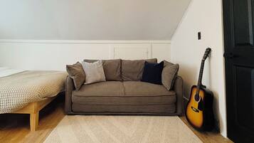 Ein kleiner, gemütlicher Raum mit einem braunen Sofa, einem hölzernen Bett und einer an der Wand angelehnten Gitarre.