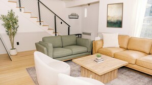 A modern living room with a staircase, green and beige sofas, a wooden coffee table, and a potted plant. - 2 Min Walk to Windham Town | Hot Tub | Fire Pit (Windham)