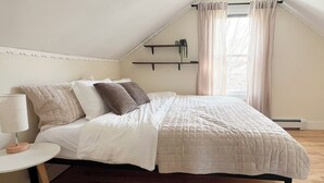 A bedroom with a bed, a bedside table, a window with curtains, a shelf with a plant, and a sloped ceiling. - 2 Min Walk to Windham Town | Hot Tub | Fire Pit (Windham)