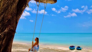 Une scène de plage avec une balançoire, un arbre et deux sacs sur le sable.