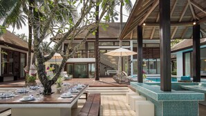 Un espace de restauration en plein air, avec des tables dressées pour le repas, entouré d’une végétation luxuriante et d’un espace piscine.