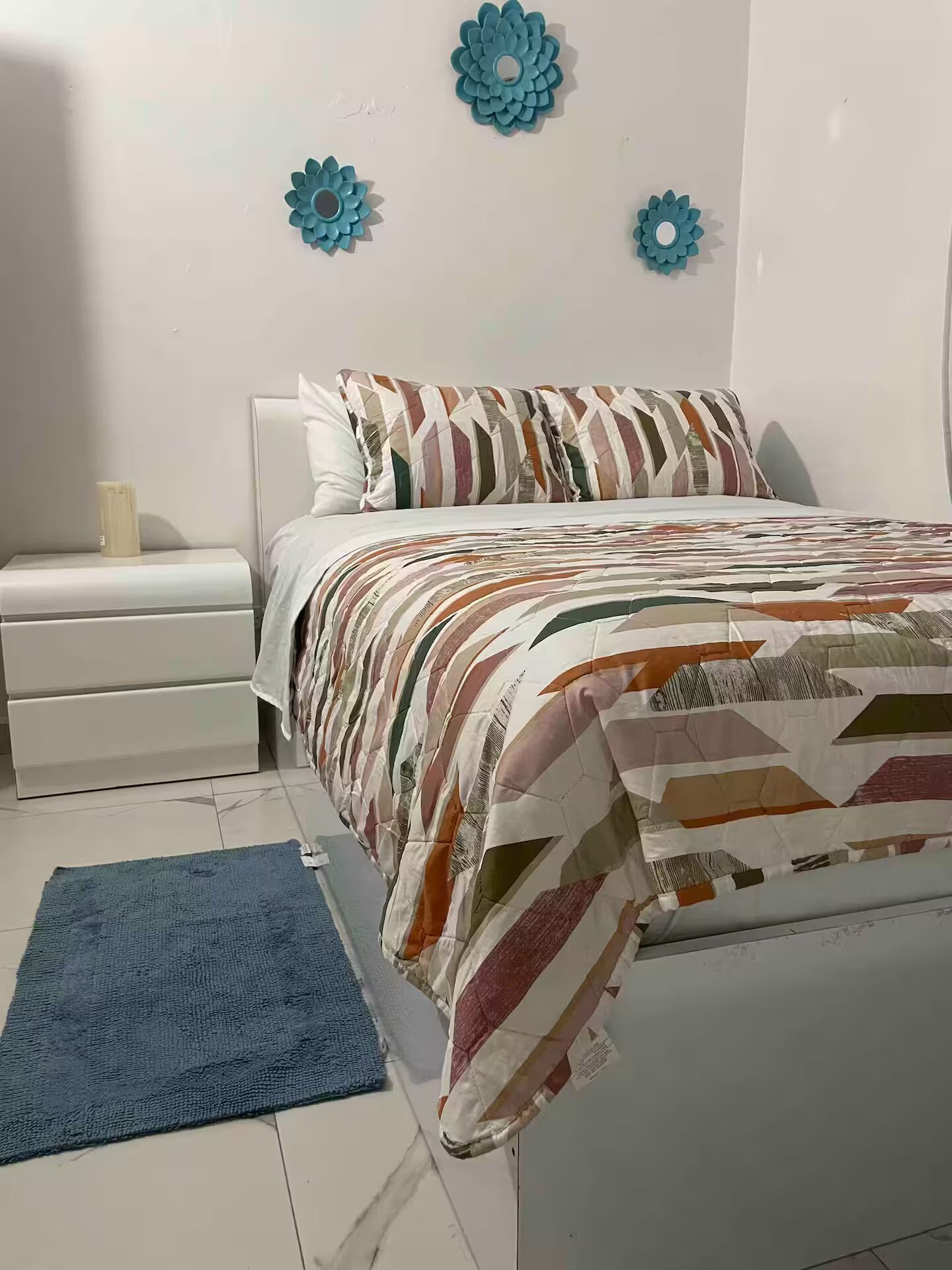 Une chambre à coucher avec un lit, une table de chevet, un tapis bleu et des œuvres d’art décoratives accrochées au mur.