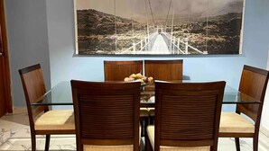 A dining area with a marble floor, wooden chairs with cushioned seats, a glass-top table, and a large painting of a bridge on the wall.