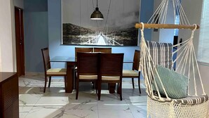 A dining area with a table and chairs, a hanging chair, and a wall-mounted painting.