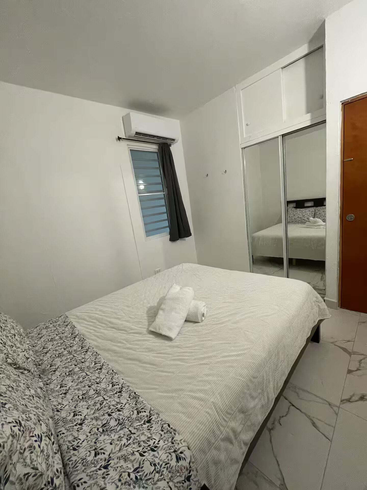Ein Hotelzimmer mit Bett, einem Vorhangfenster, einem Kleiderschrank und einem Spiegel.