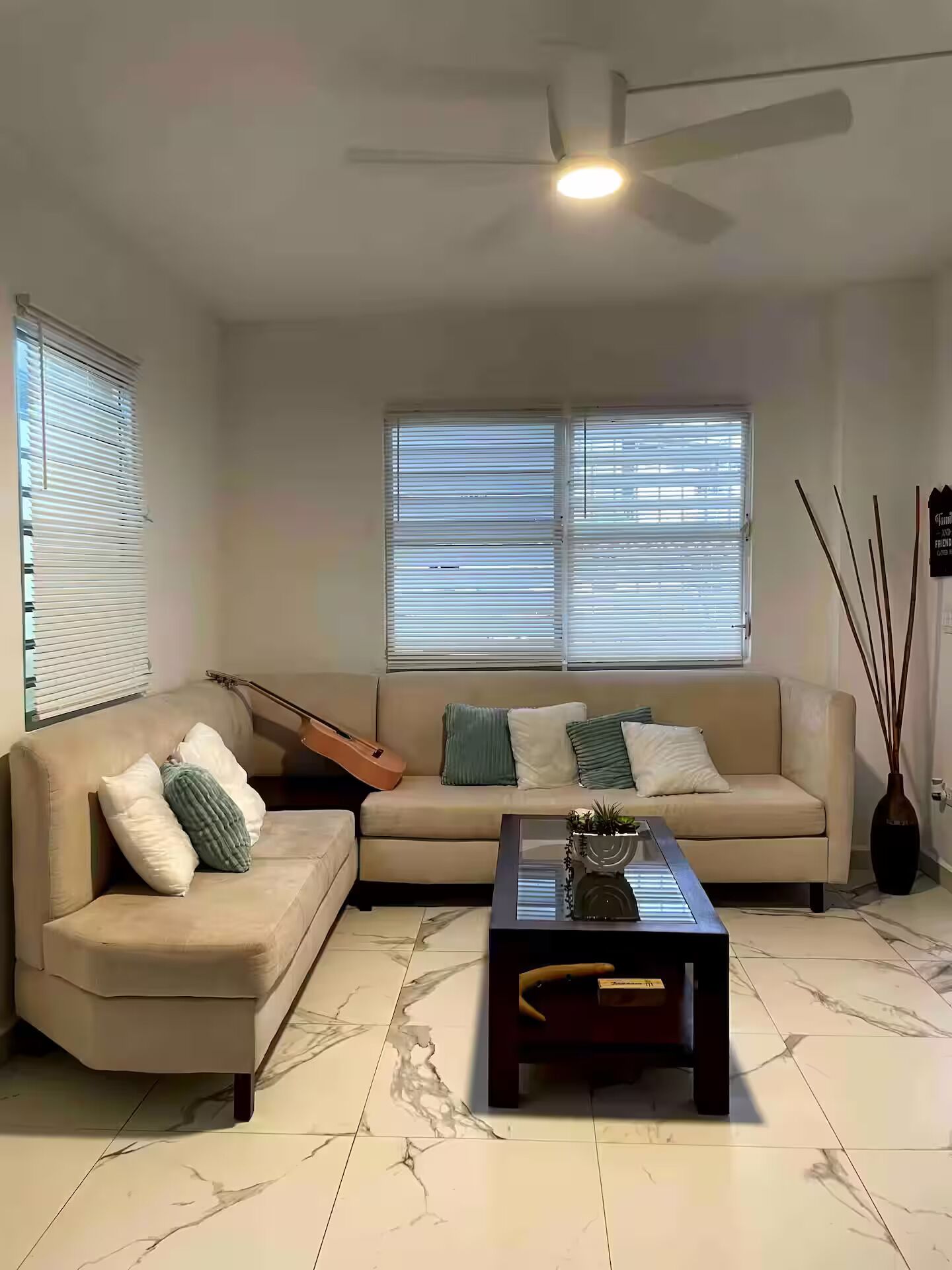 A living room with a sofa, a coffee table, a guitar, and a ceiling fan.