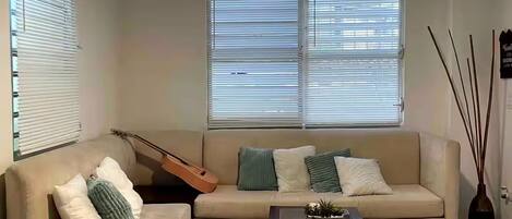 A living room with a sofa, a coffee table, a guitar, and a ceiling fan.