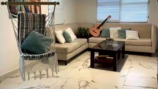 A living room with a hammock chair, a sofa, a coffee table, and a guitar.