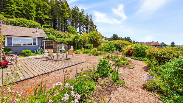 A wooden deck with outdoor furniture, surrounded by a garden with various plants and flowers.