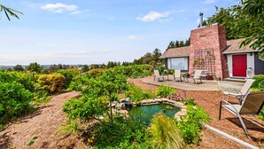A house with a brick exterior, a red door, and a patio with outdoor furniture. There is a small pond in the garden.