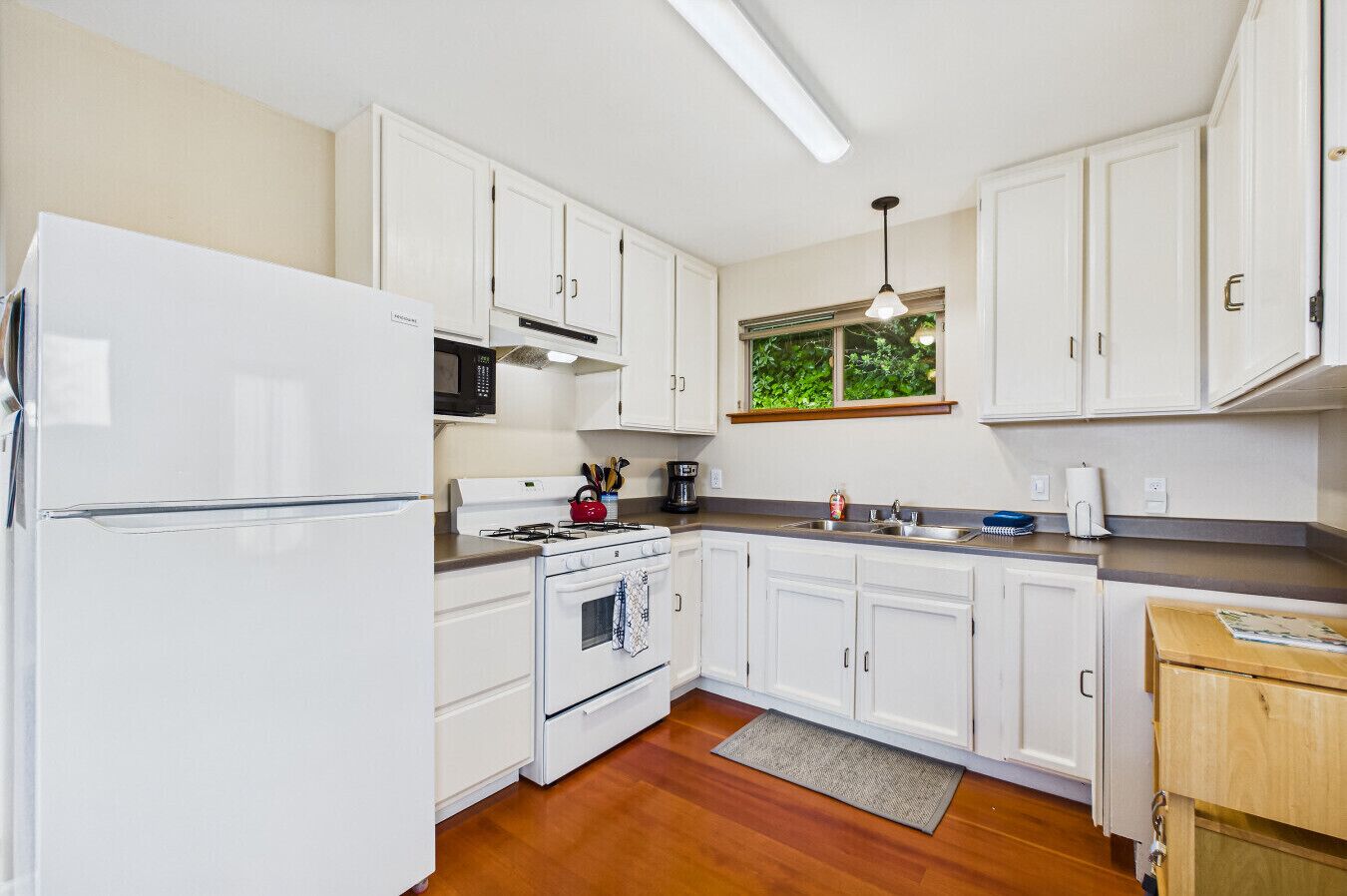 A compact kitchen with white cabinets, a microwave, a stove, and a sink.