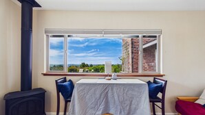 A room with a large window, a table with chairs, a red bench, and a black stove.